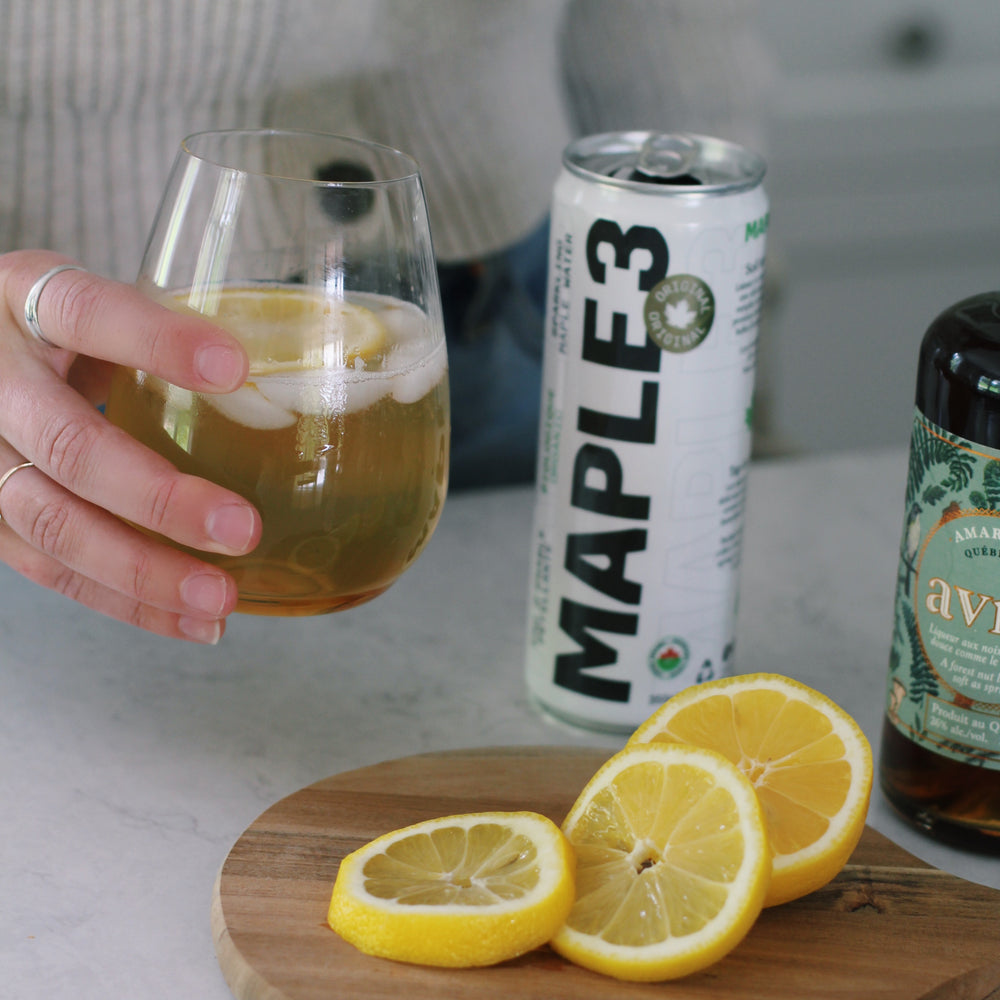 Holding a glass of Maple Amaretto Sour made with sparkling Maple 3 water.