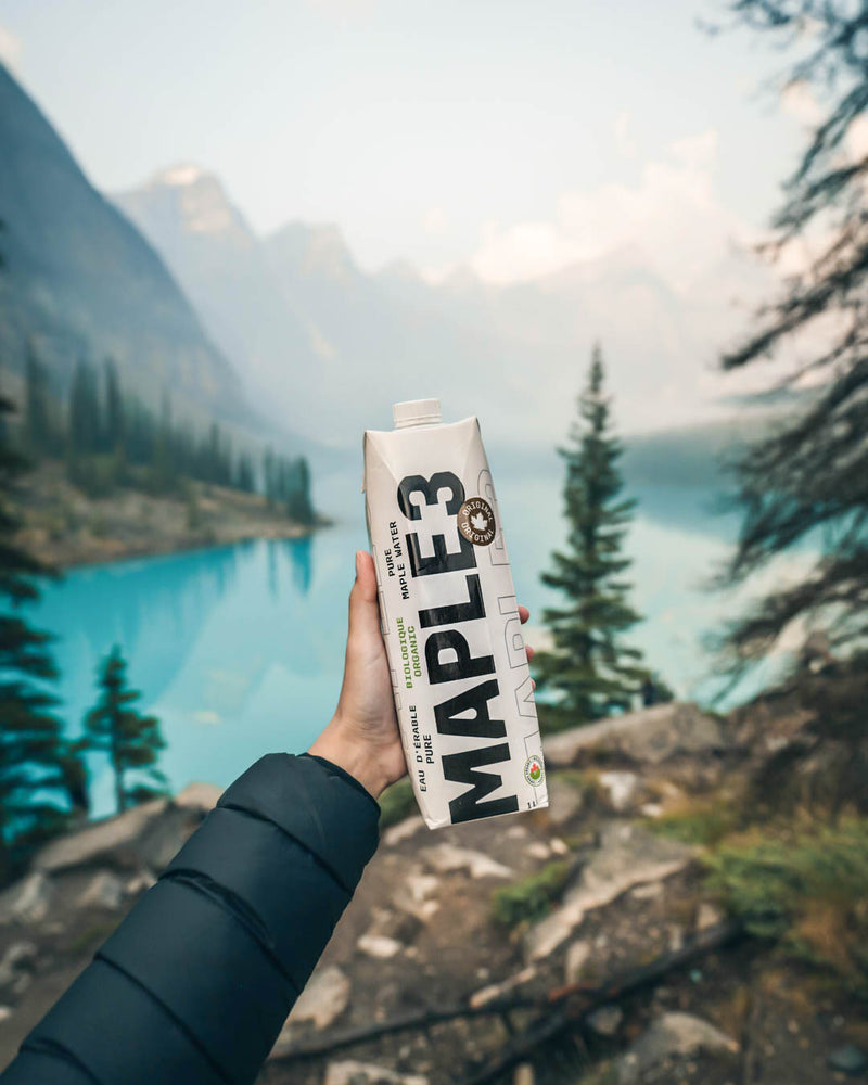 Someone holding pure maple water 1L in front of a blue lake in British Columbia