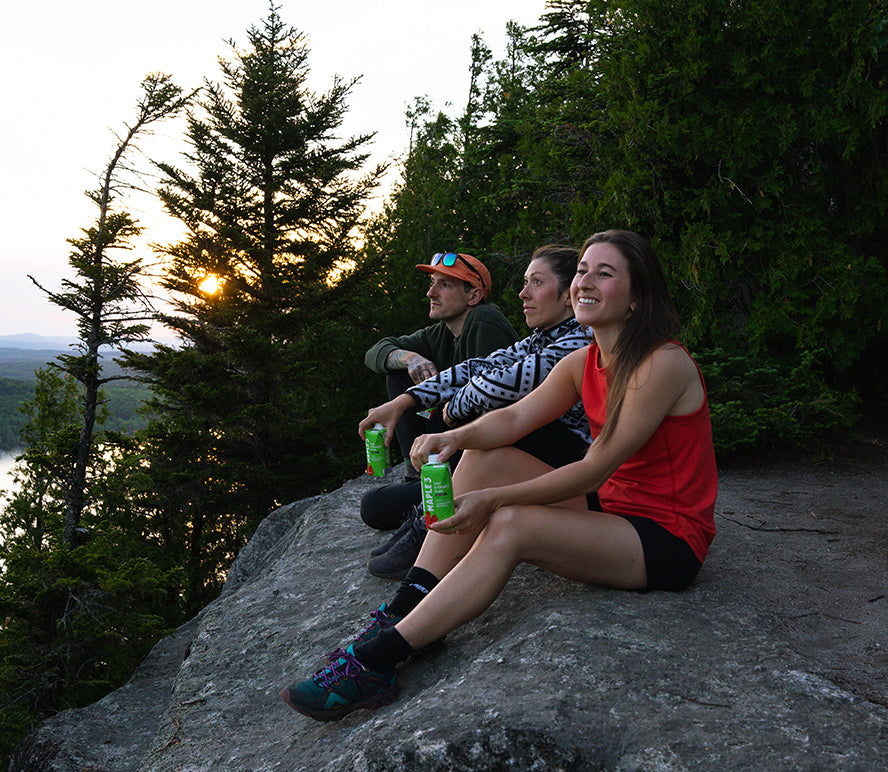 Three friends watching the sunset on top of a mountain with organic maple water.